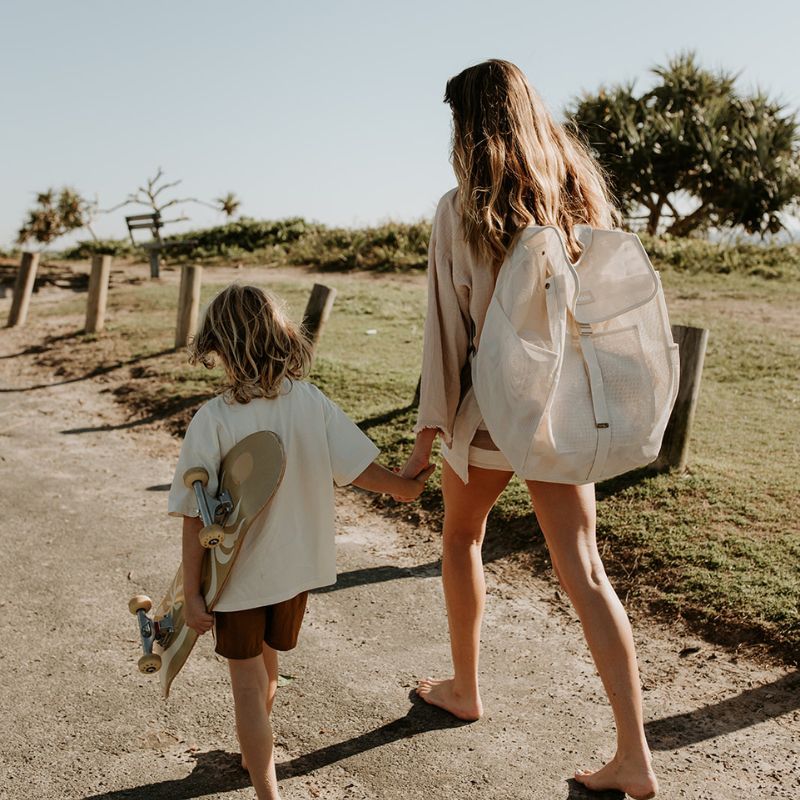 Mum and son walking to the beach, with mum carrying her Sande Beach Hauler mesh beach backpack in neutral Sand colour.