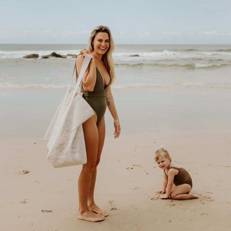 A mother at the beach with her young daughter. She is carrying the Sande™ original oversized Beach Hauler™ mesh beach bag.