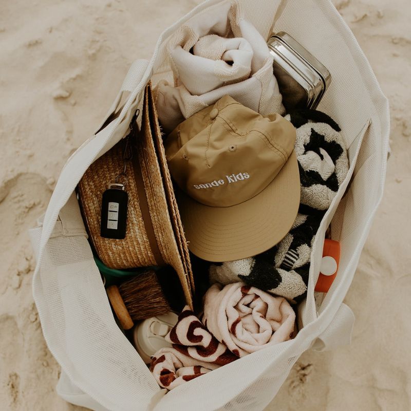 The oversized Sande™ Beach Hauler mesh beach bag packed with beach essentials such as towels, sunscreen, hats, and water bottles showcasing the spacious interior and functionality of this oversized beach bag. Perfect for family outings and beach days.
