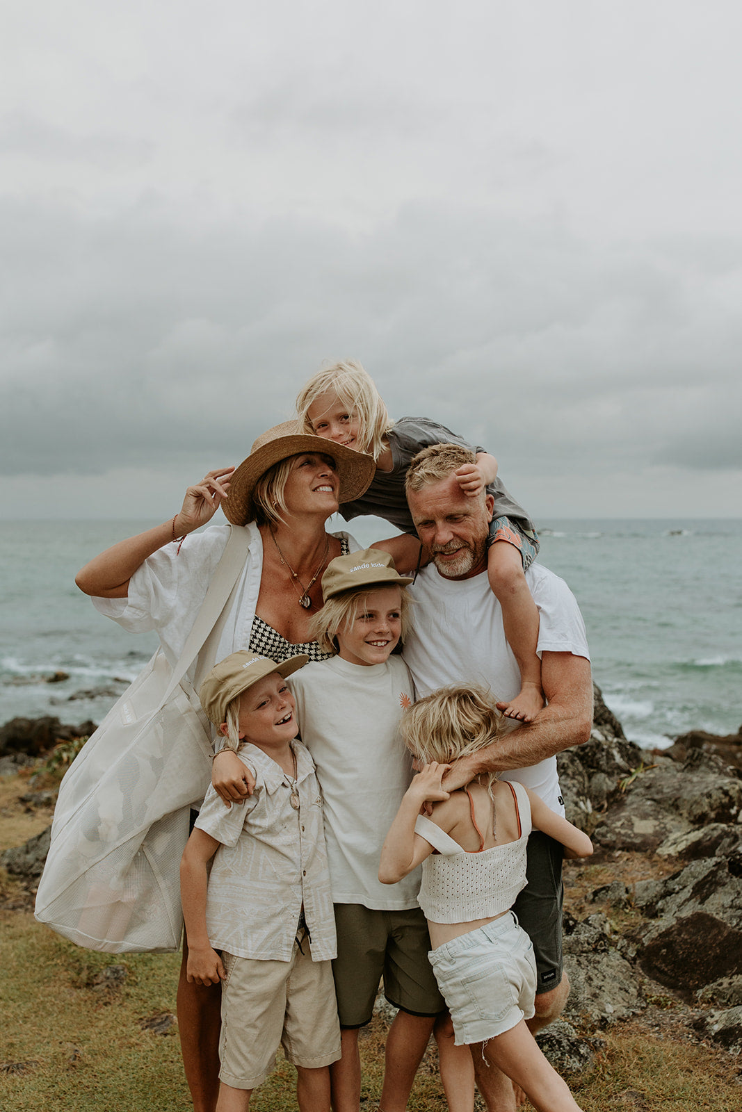 The Sande founder Kim, her husband and 4 blonde children huddled together at the beach for a family photo.