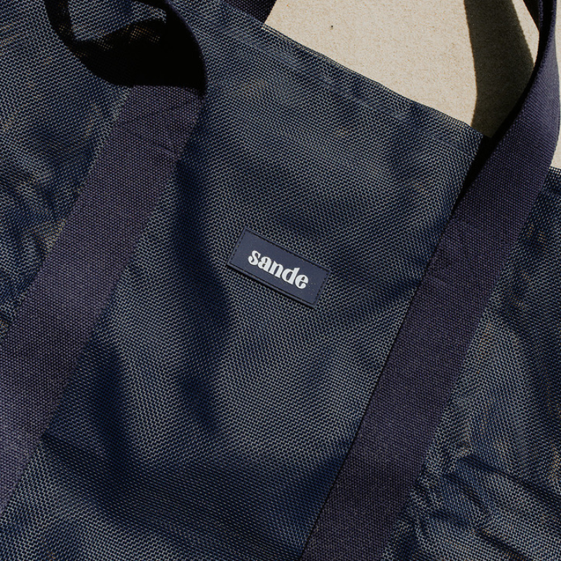 Close-up of the high-quality features of the Sande Beach Hauler mesh beach bag in Deep Sea Navy. Highlights the durable PVC mesh fabric, thick cotton straps, and silicone Sande logo.