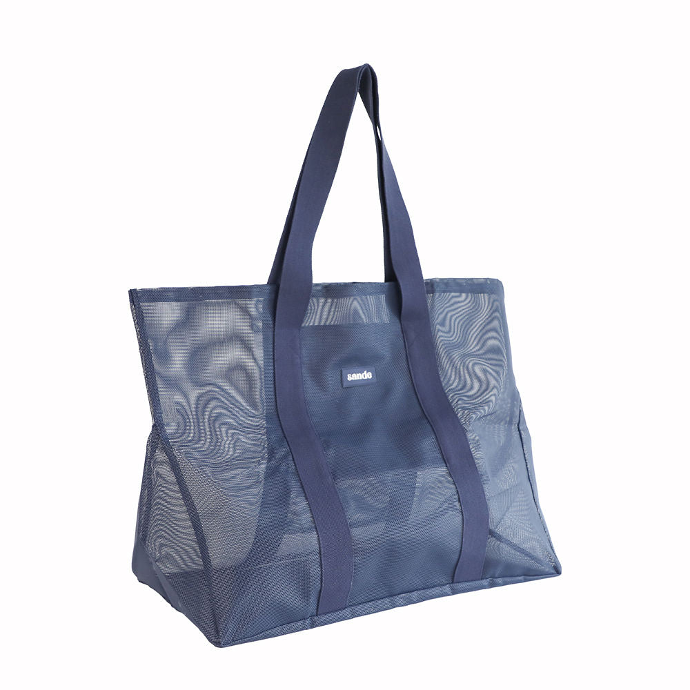 Oversized Sande Beach Hauler mesh beach bag in Deep Sea Navy, displayed in a studio setting. Positioned at a 45 degree angle to highlight the mesh detail, thick cotton straps, and silicone Sande logo. Set against a white background.