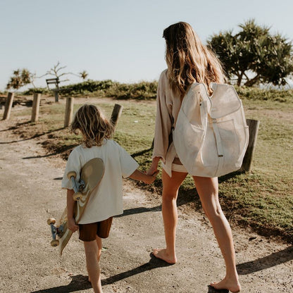 Mum and son walking to the beach, with mum carrying her Sande  Beach Hauler mesh beach backpack in neutral Sand colour.