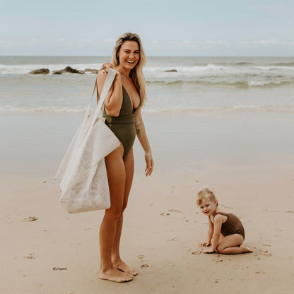 A mother at the beach with her young daughter. She is carrying the Sande™ original oversized Beach Hauler™ mesh beach bag.