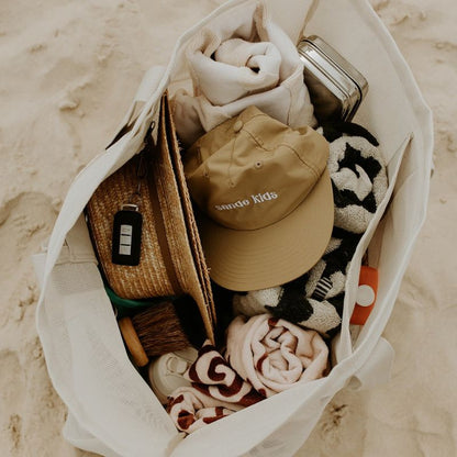 The oversized Sande™ Beach Hauler mesh beach bag packed with beach essentials such as towels, sunscreen, hats, and water bottles showcasing the spacious interior and functionality of this oversized beach bag. Perfect for family outings and beach days.