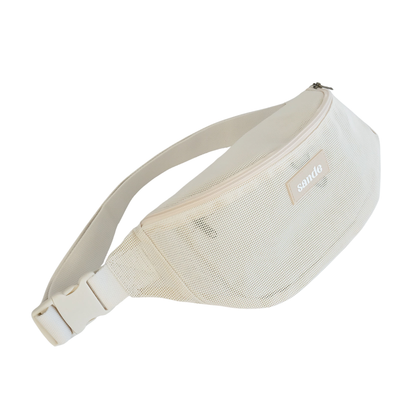 45º angled view of the Sande Essentials Crossbody Bag in Sand on a white background, highlighting the mesh fabric, silicone Sande logo, YKK zip, YKK secure clip and adjustable strap. The overall silhouette reflects a classic bum bag shape.