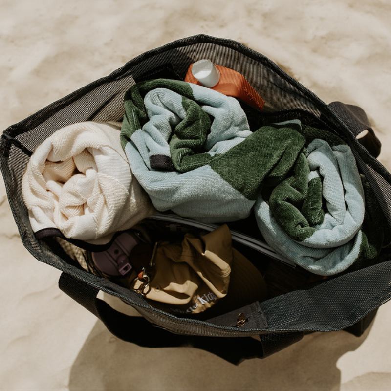 Top view of the Sande Beach Hauler - Mini, a large mesh beach bag in Deep Sea Navy resting on the sand. This image highlights the large capacity of the  mesh beach bag, showcasing its ability to fit beach towels, hats, sunscreen, snacks, water bottles, and valuables‚Äîmaking it the perfect beach bag for all your essentials.