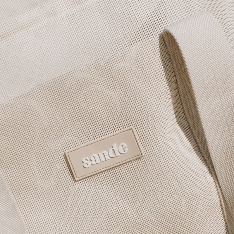 Sande™ Beach Hauler‚ featuring durable neutral PVC mesh fabric and thick cotton webbing strap in neutral, designed for optimal comfort and style for beach trips and family adventures. Silicone Sande logo.