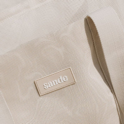 Sande™ Beach Hauler‚ featuring durable neutral PVC mesh fabric and thick cotton webbing strap in neutral, designed for optimal comfort and style for beach trips and family adventures. Silicone Sande logo.