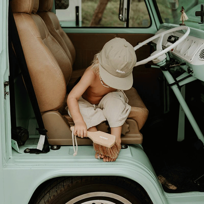 Little boy siting at the door of a vintage Kombi Van using the Sande sand brush to sweep sand from his feet.