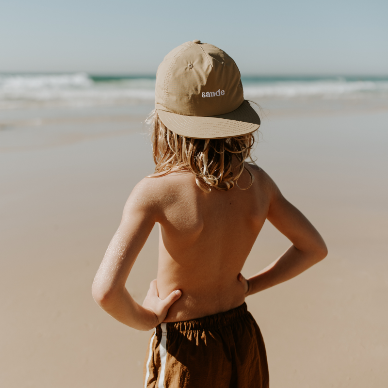 A little boy at the beach, with the ocean in the background, standing with his hands on his hips. He is wearing the Sande cap on backwards, showcasing the embroidered Sande  logo.
Cap is lightweight, fast-drying nylon. Perfect for outdoor adventures.